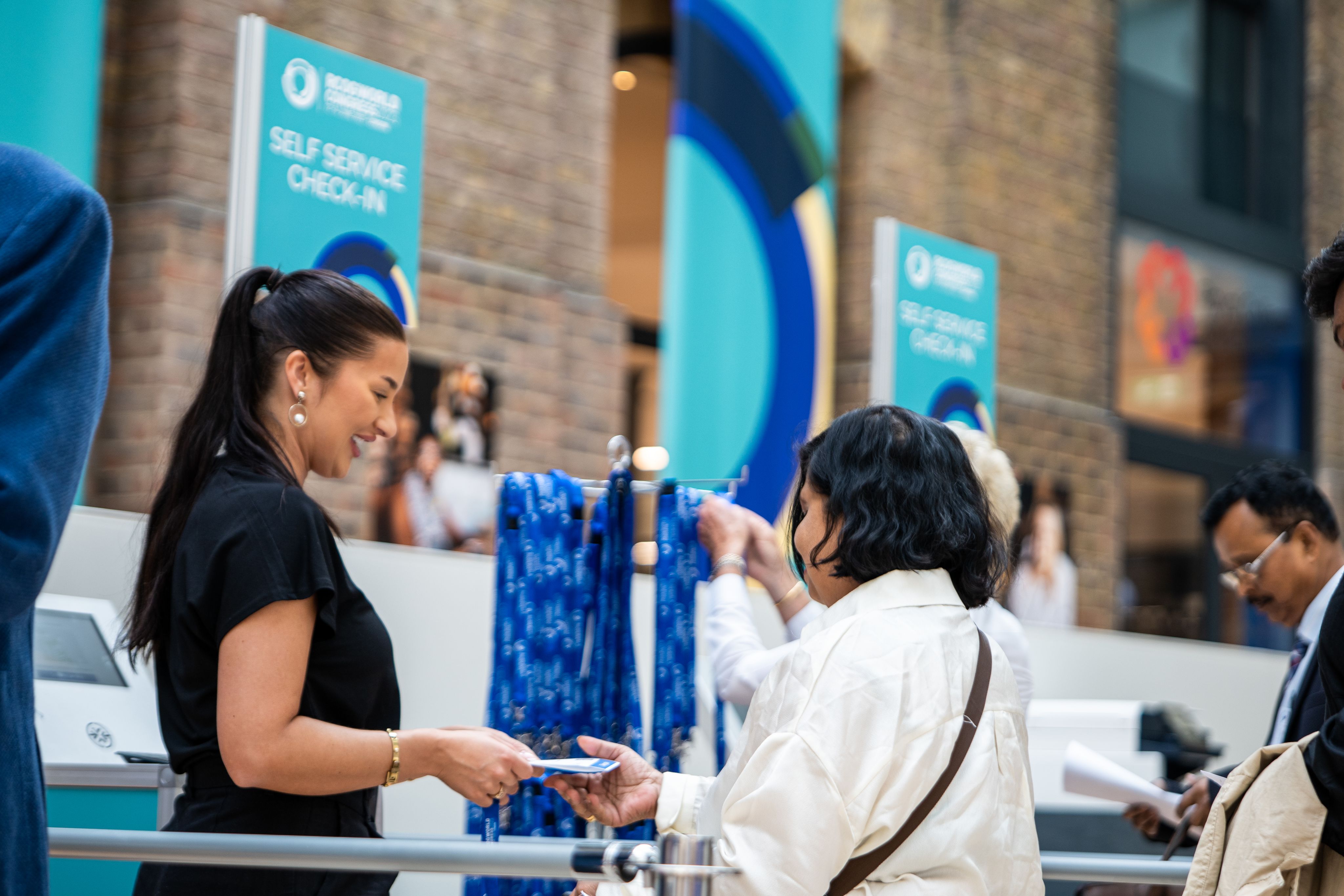 Two women exchange lanyard at RCOG World Congress 2023 in atrium of RCOG Union Street building.