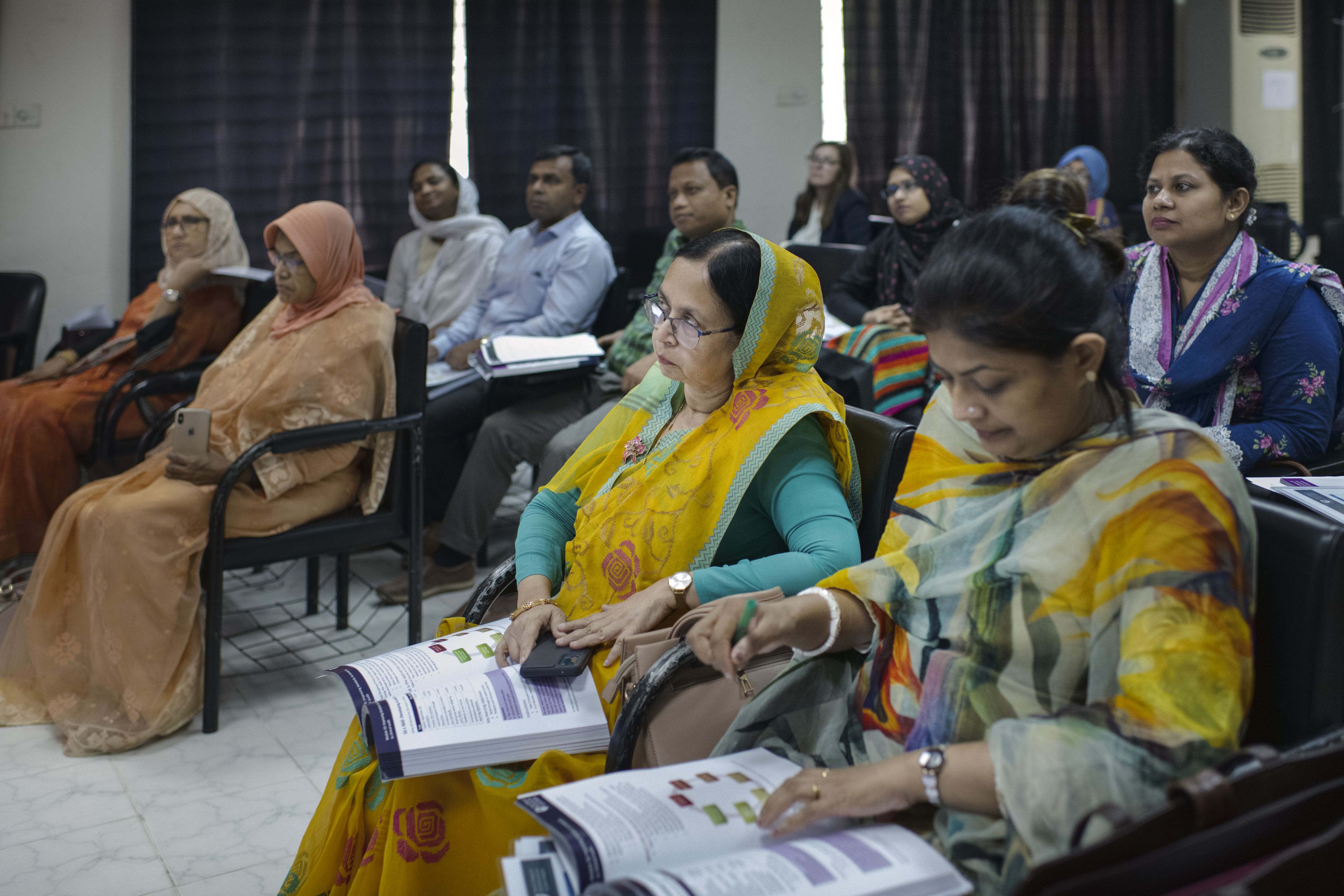 Women at the RCOG Essential Gynaecological Skills training in Bangladesh, sitting in chairs with training booklets on their laps