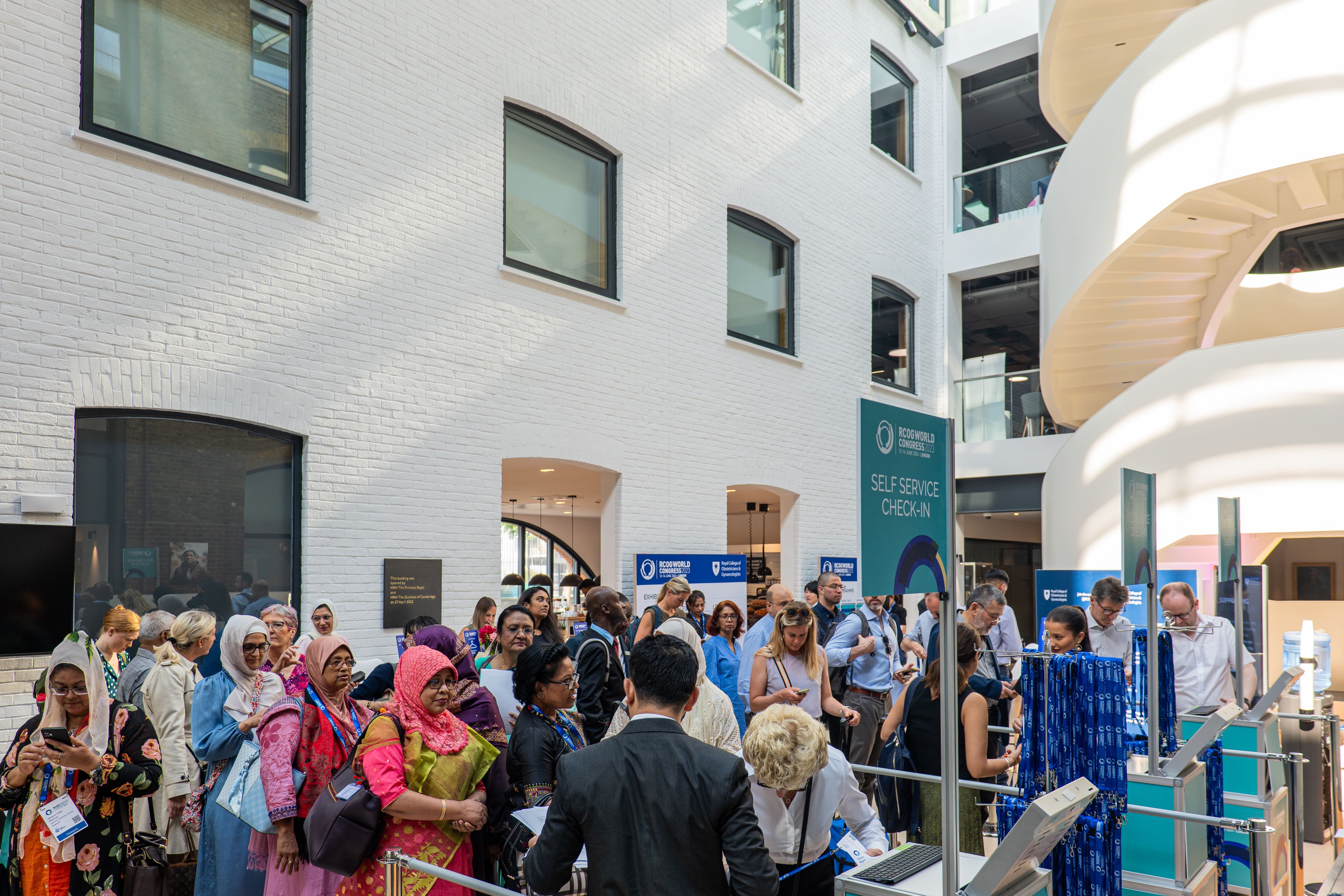 People gather for RCOG World Congress 2023 in atrium of RCOG Union Street building, with white spiral staircase.