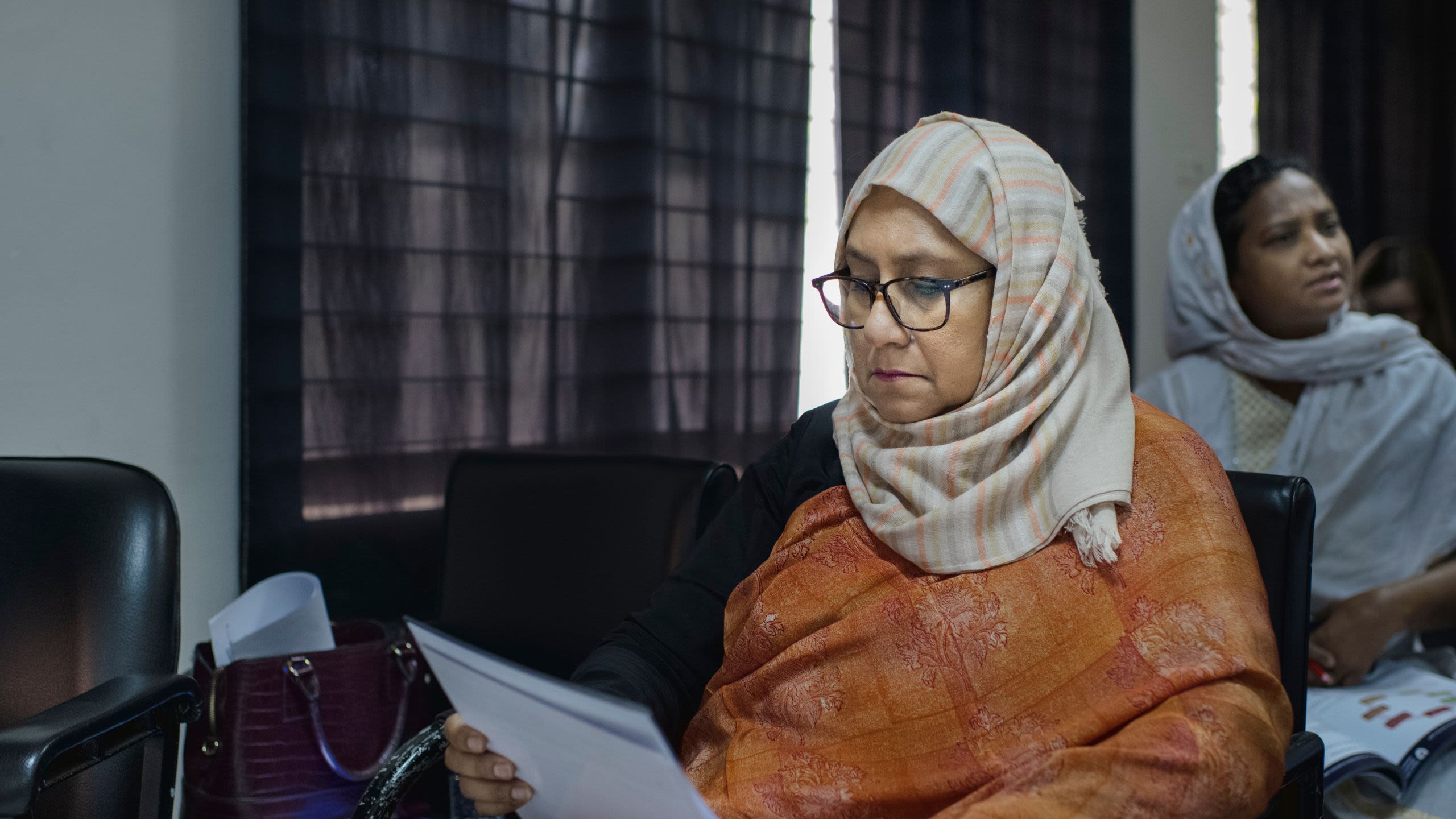 A woman wearing a headscarf sits down and reads from a sheet of paper during Essential Gynaecological Skills training in Bangladesh