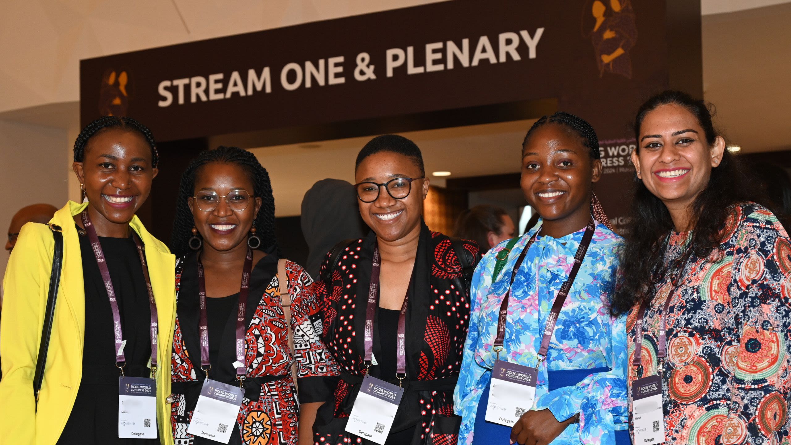 A group of 5 women at RCOG World Congress 2024 in Oman. They are standing in a line and smiling at the camera