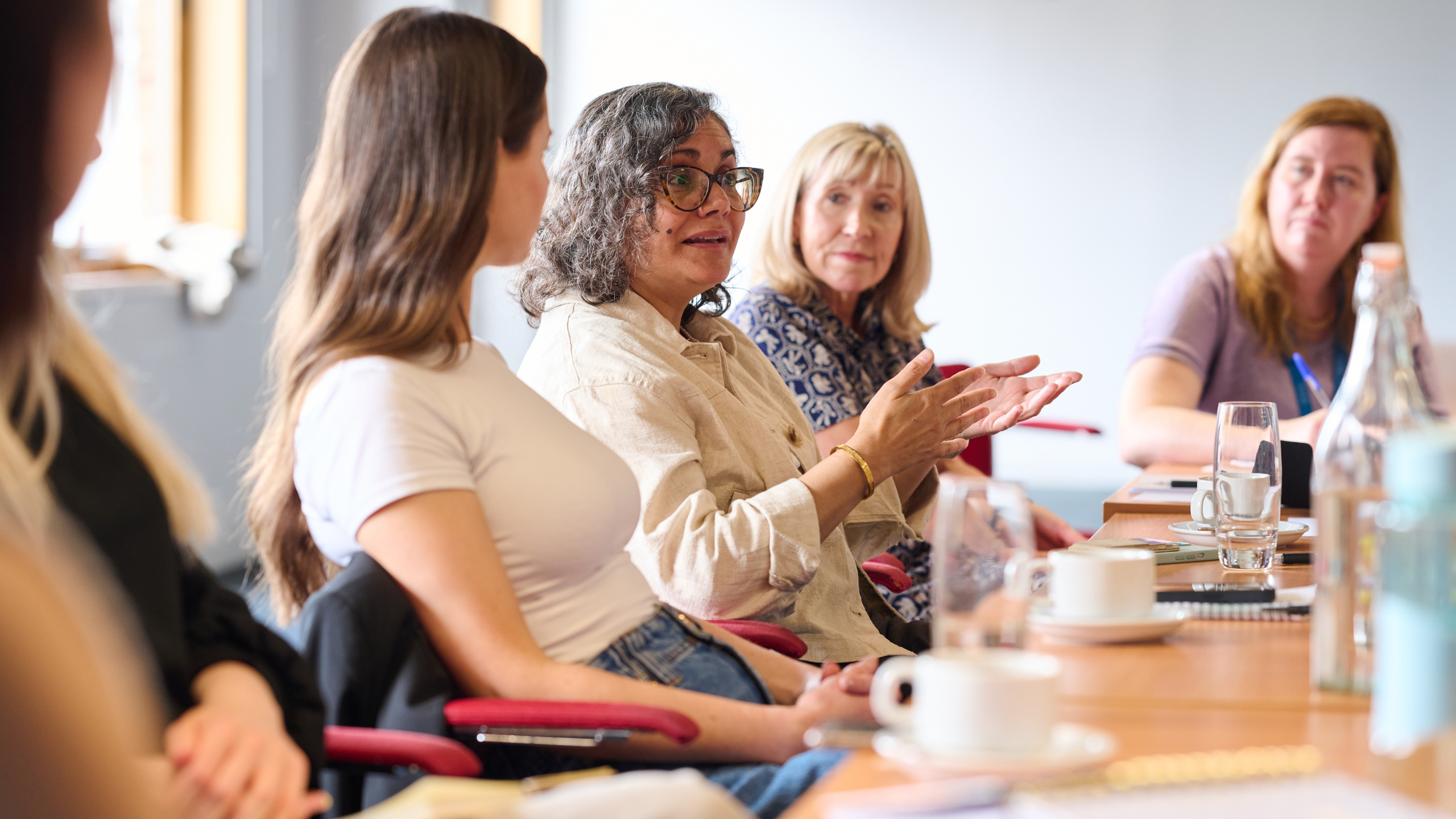 A photo of women at a focus group for the Waiting for a Way Forward report. One woman in the middle of the photo is talking and gesturing with her hands.